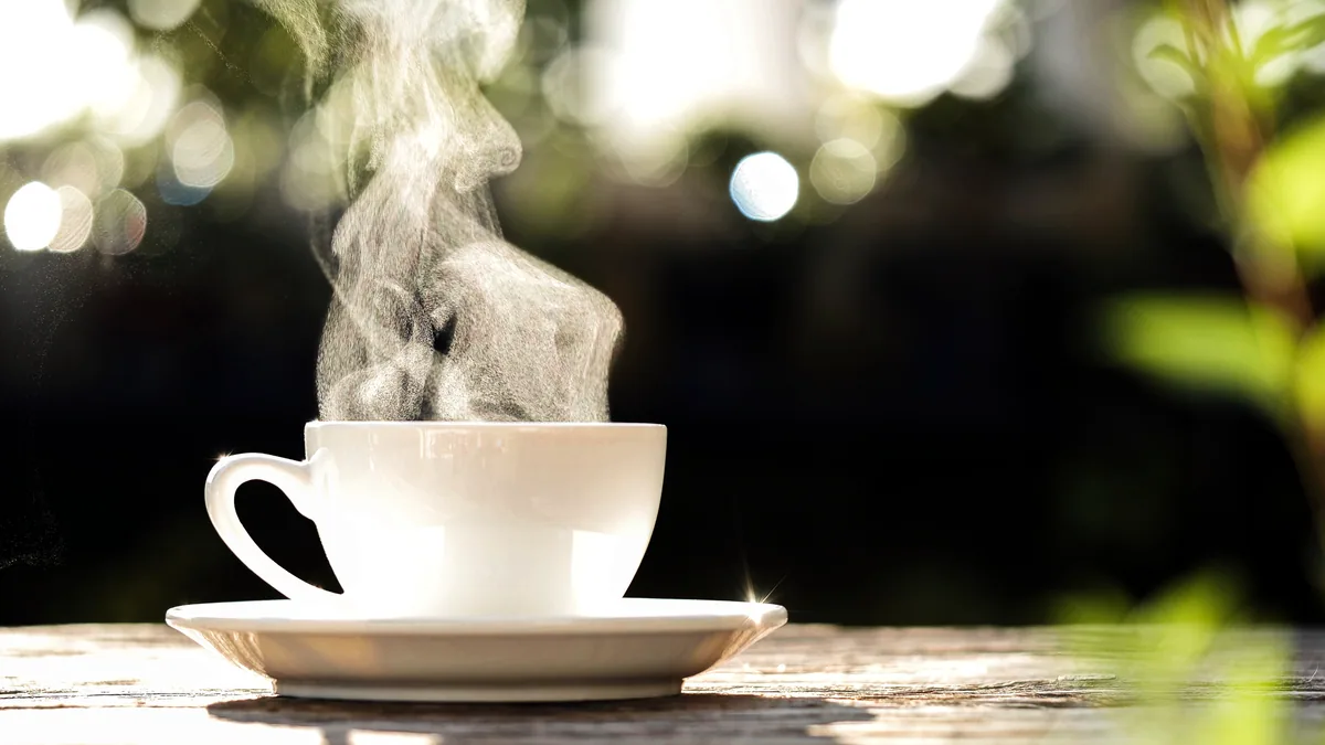 A white ceramic mug of black coffee releasing a thin wisp of steam on a kitchen table.