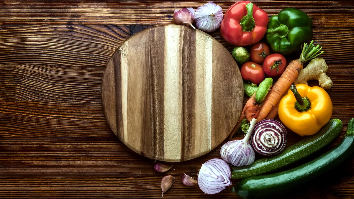 A colourful mix of leafy greens, orange carrots, and red peppers arranged on a wooden cutting board.